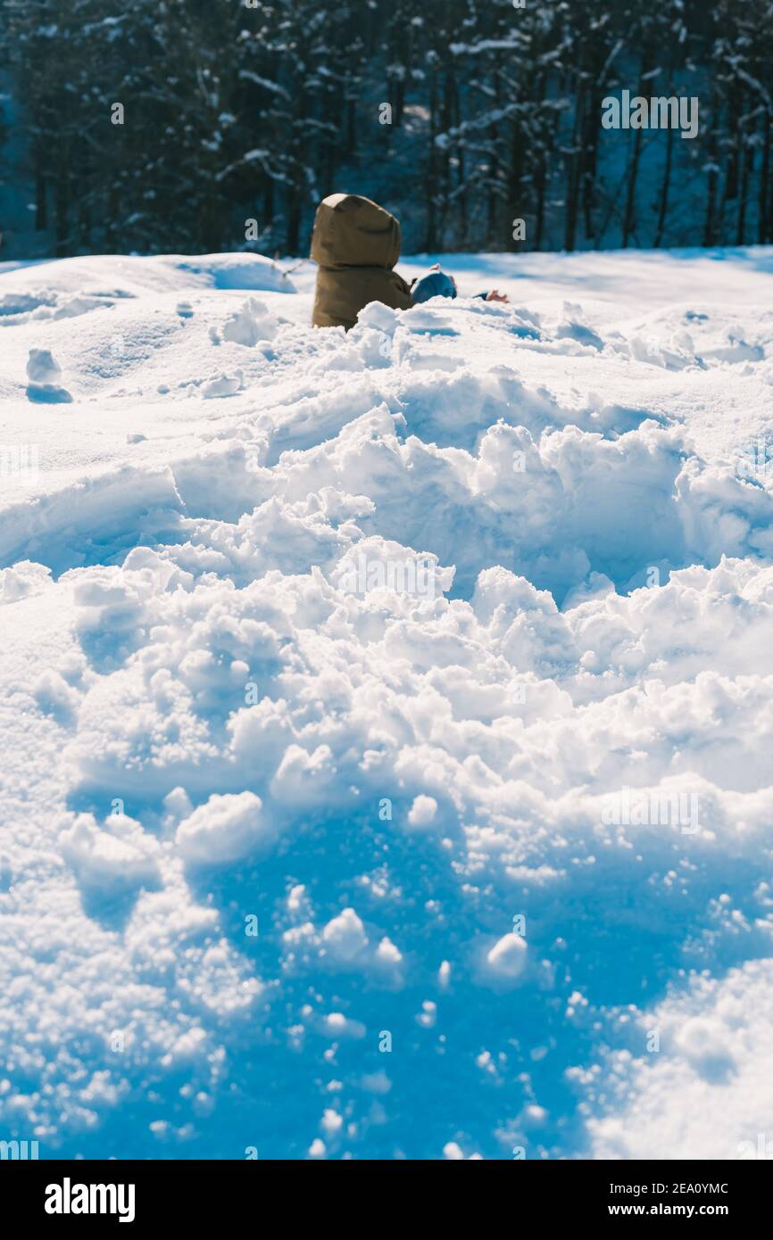 Un cliché vertical d'un enfant dans une veste matelassée jouant dans la neige pendant une journée d'hiver ensoleillée Banque D'Images