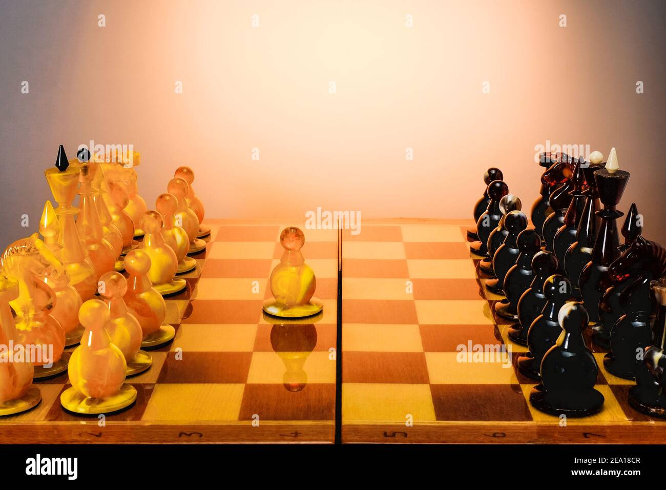 Jeu d'échecs avec des figures d'échecs ambrées sur le plateau sur table blanche, d'abord déplacer E2 E4, avec fond dégradé or. Banque D'Images