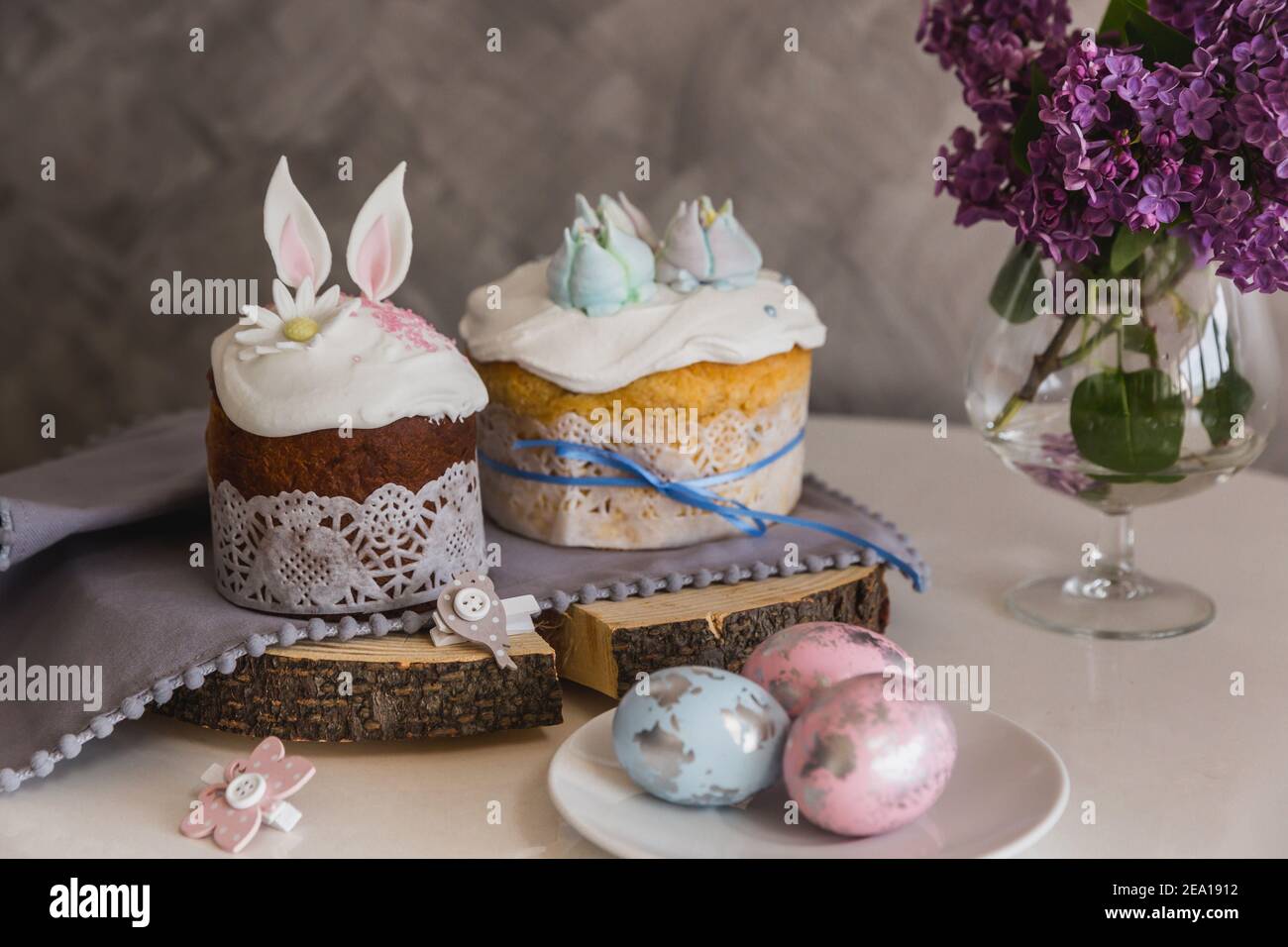 Gâteaux de Pâques en bois décorés avec des oreilles de lapin, œufs sur le plateau au premier plan, lilas sur le fond. - pain de Pâques traditionnel Kulich, paska. T Banque D'Images