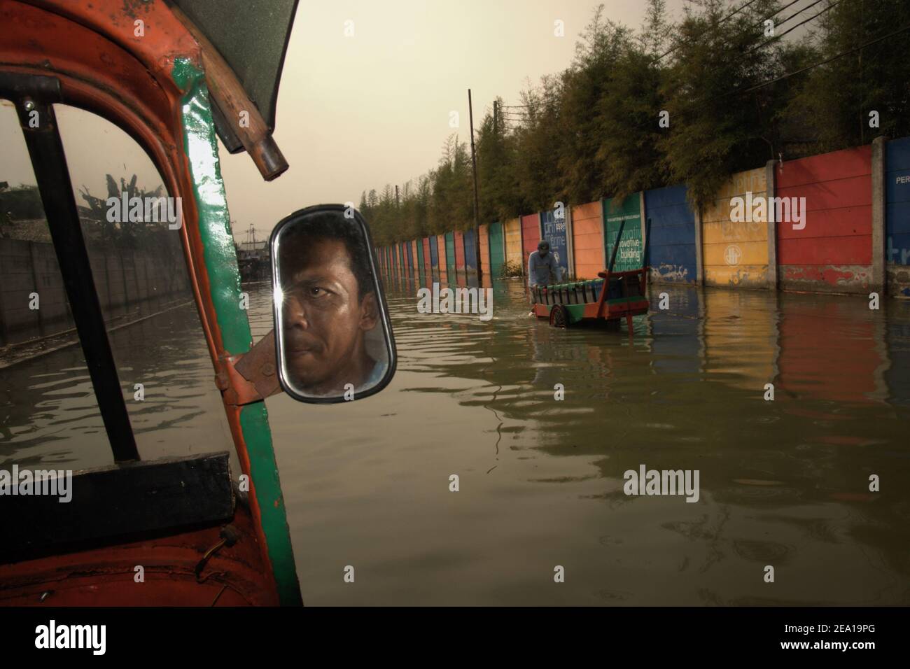 Un chauffeur d'autopousse transportant des passagers dans une rue inondée d'eau de mer, passant par un ambulant d'eau douce dans la région de Muara Baru, dans la zone côtière de Jakarta, en Indonésie. Banque D'Images