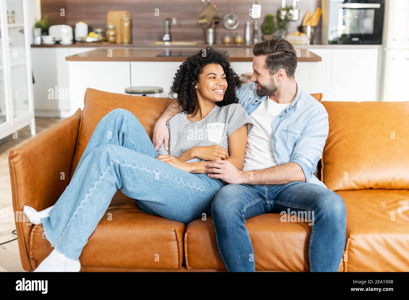 Charmant couple multiracial dans embrasse dans le salon confortable à la maison. Le couple interracial hilarant aime le temps ensemble à la maison assis sur le Banque D'Images