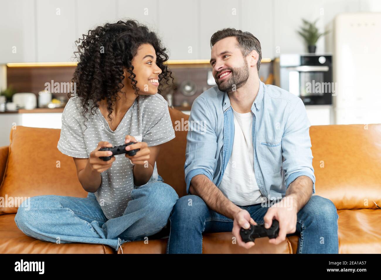 Un couple multiracial excité aime jouer au jeu vidéo, une femme africaine et un homme caucasien tiennent des joysticks sans fil se regarder les uns les autres prêts à combattre Banque D'Images