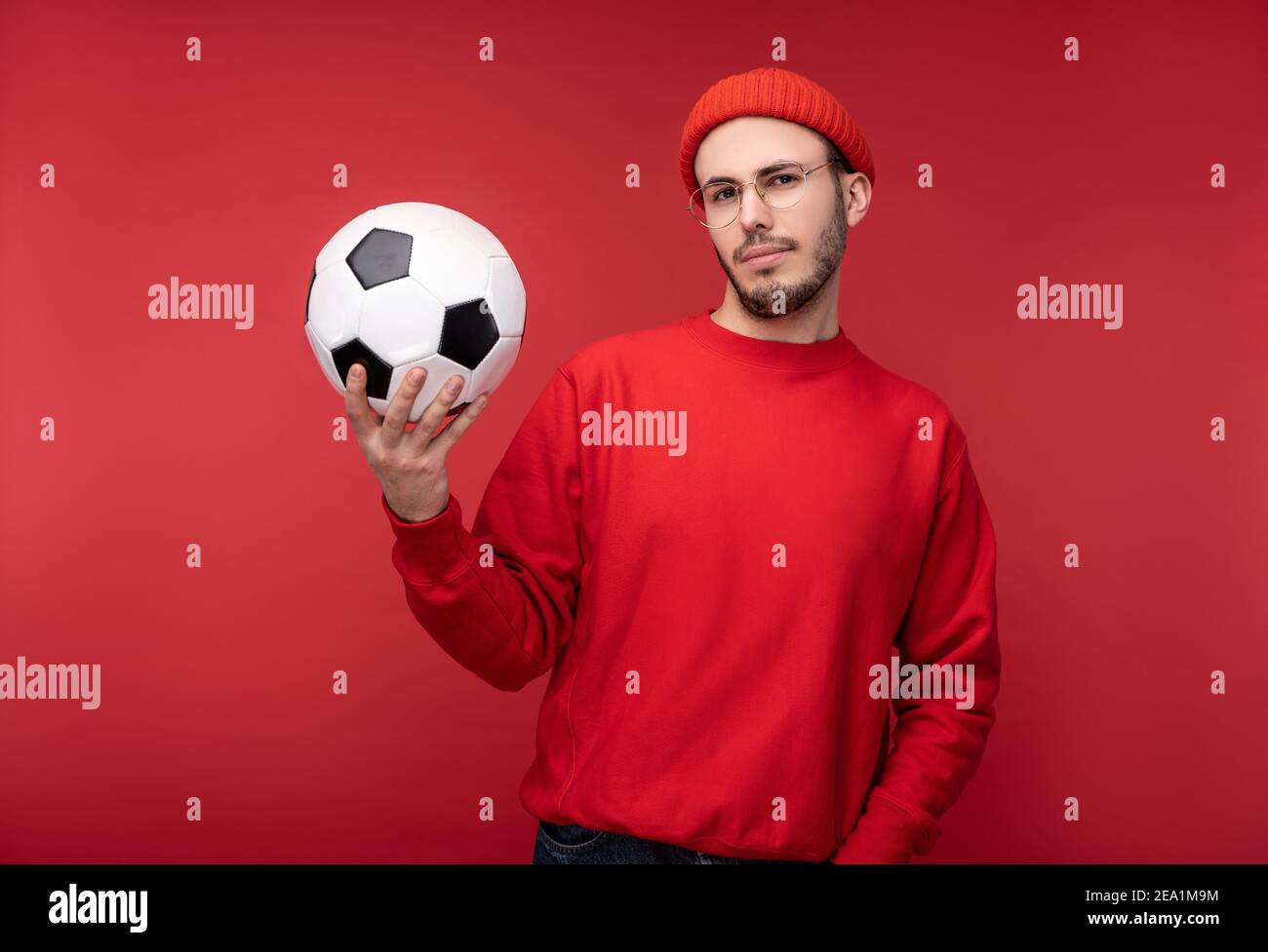 Photo d'un homme attrayant avec une barbe en lunettes et des vêtements rouges. L'homme heureux tient le ballon, isolé sur fond rouge Banque D'Images