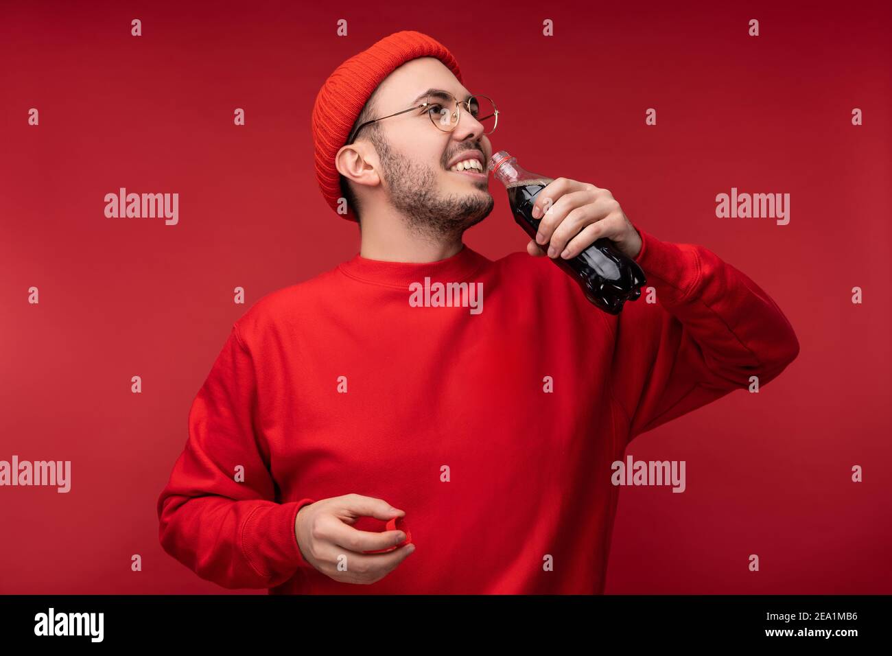 Photo d'un homme attrayant avec une barbe en lunettes et des vêtements rouges. Un homme heureux tient une boisson, isolé sur fond rouge Banque D'Images