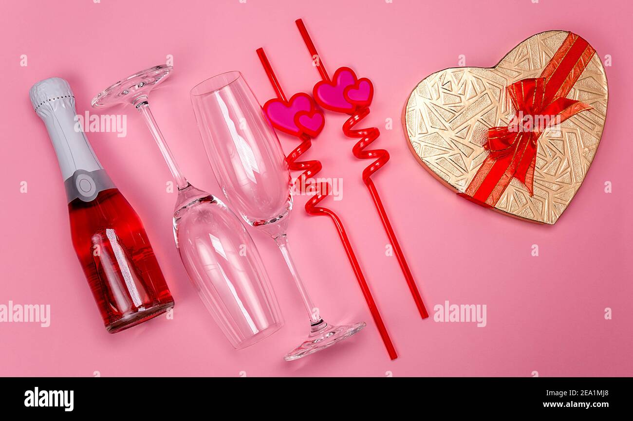 Deux verres à champagne avec pailles à boire en plastique rouge avec coeurs, boîte cadeau et bouteille de champagne rouge sur fond rose. Banque D'Images