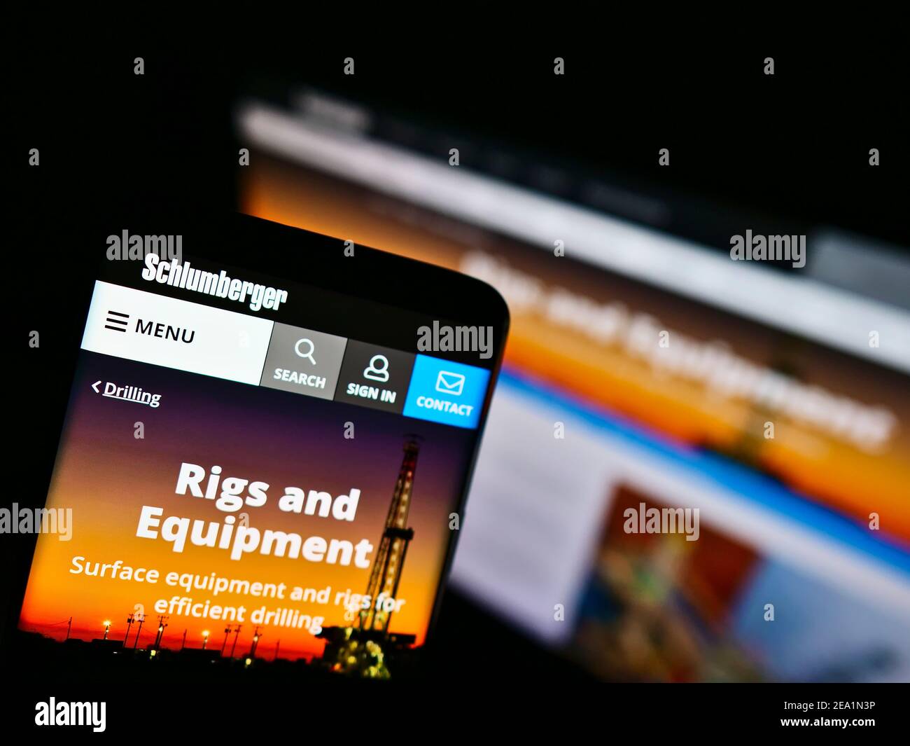 Smartphone avec le site Web d'entreprise et le logo de la société de services pour champs pétrolifères Schlumberger sur l'écran devant le moniteur. Concentrez-vous sur l'affichage du téléphone mobile. Banque D'Images