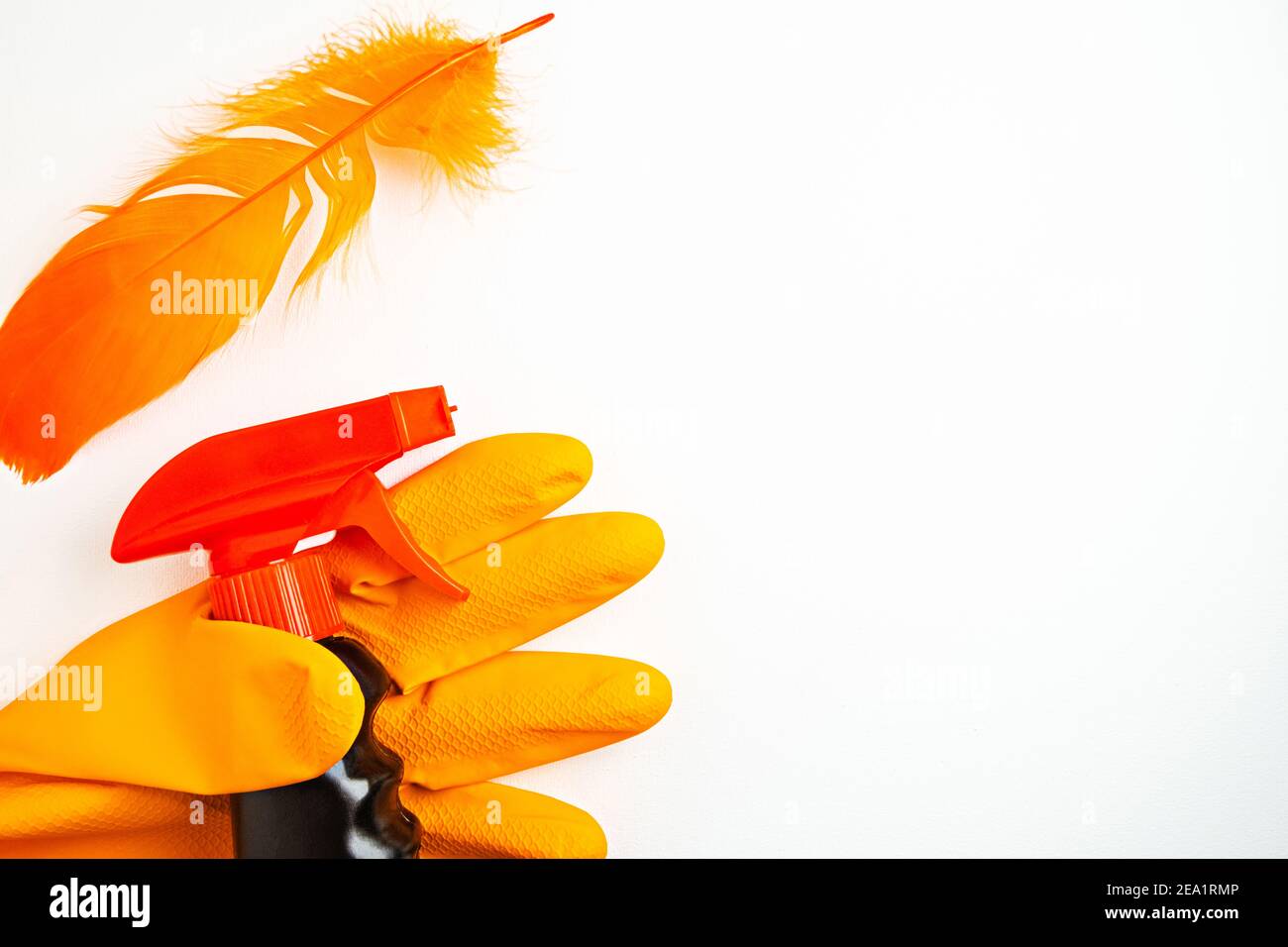 Spray nettoyant noir à la main dans un gant orange et une plume orange sur fond blanc. Concept de nettoyage, de propreté et de produits chimiques domestiques. Copier la flèche Banque D'Images