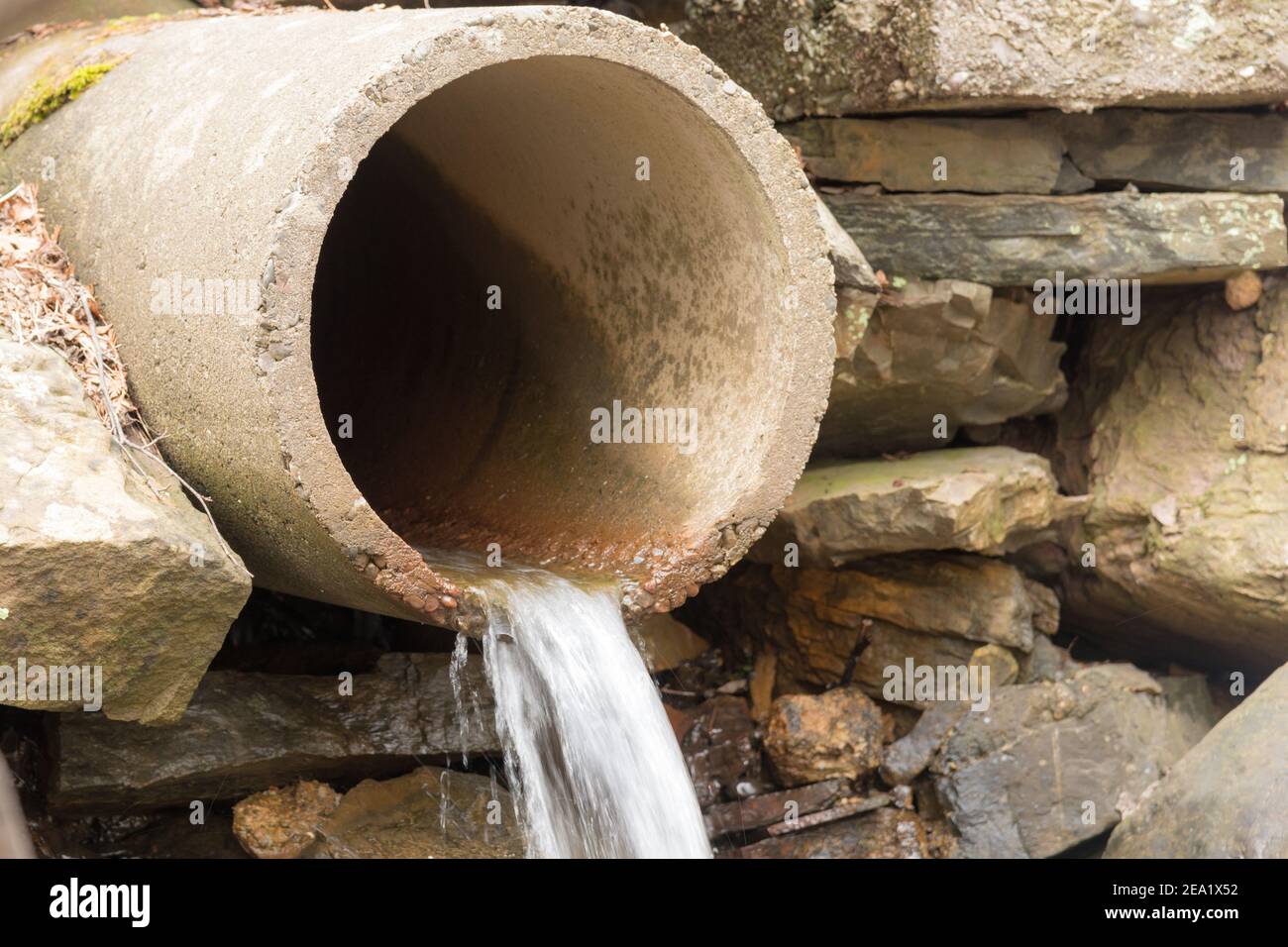 Un ancien tuyau d'évacuation en béton dans un mur en pierre. Un peu d'eau  s'écoule du tuyau. La mise au point se fait sur le bord le plus proche  Photo Stock -