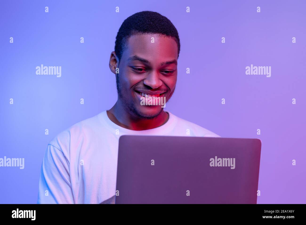 Beau sourire Black Programmer Guy travail en ligne sur l'ordinateur portable dans Néon Banque D'Images