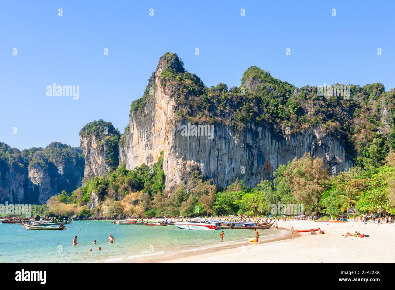 Les vacanciers apprécient la plage et la mer à l'ombre d'une immense formation de rochers sur la plage de Railay, près de Krabi, en Thaïlande Banque D'Images