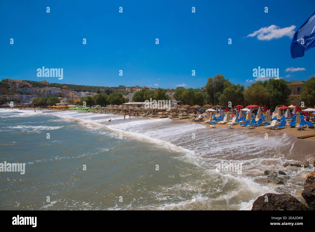 Kalyves,CRÈTE-GRÈCE:JUILLET 5 2017.la plage Kalyves.Rouge chaises longues et parasols, les gens sur les maisons de fond de village. Banque D'Images