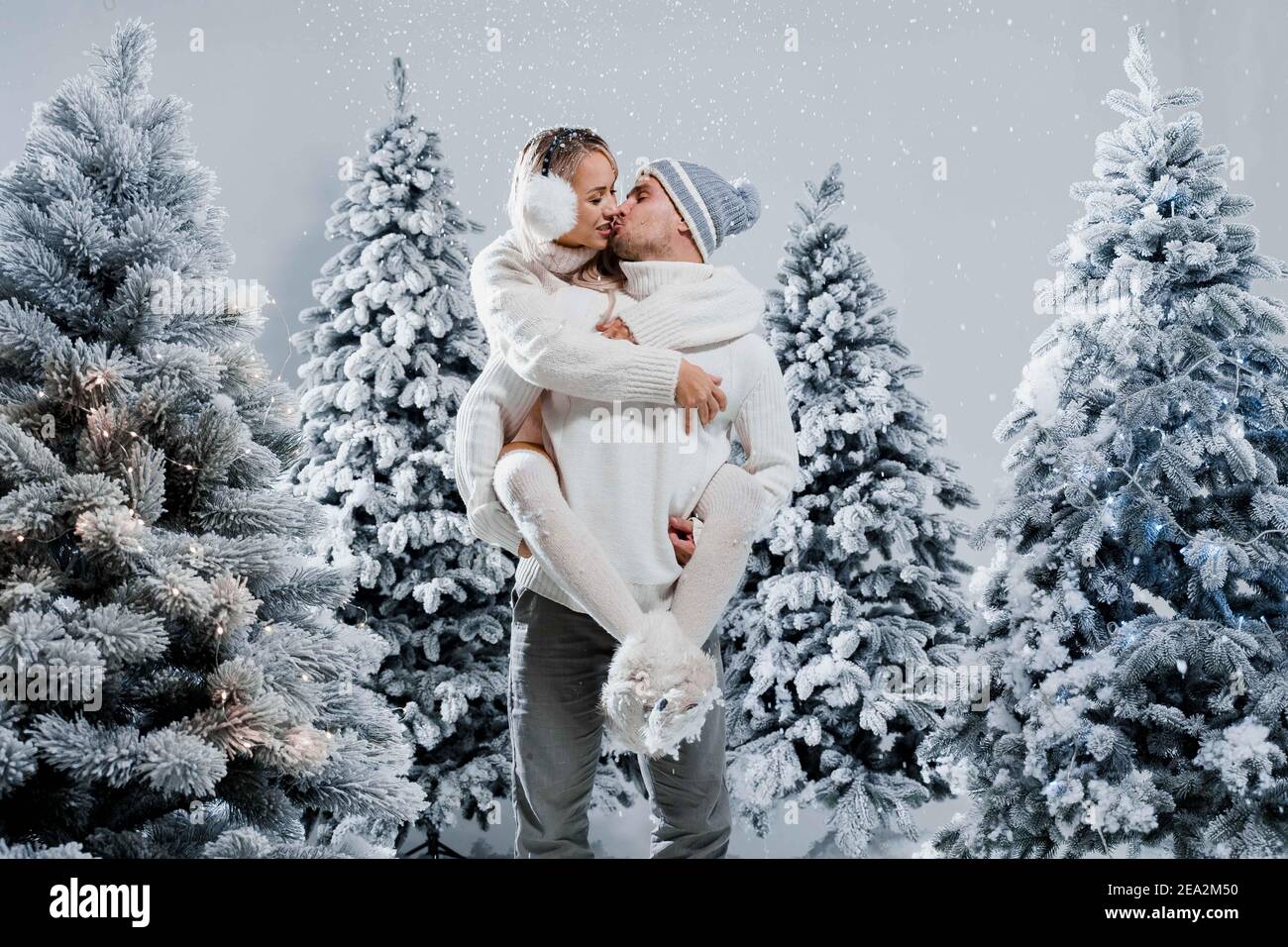 Couple baiser et câlin. L'homme tient une fille près des arbres de noël en  hiver. Célébration du nouvel an. Les gens ont pleuré en portant des casques  à fourrure, des chapeaux, un