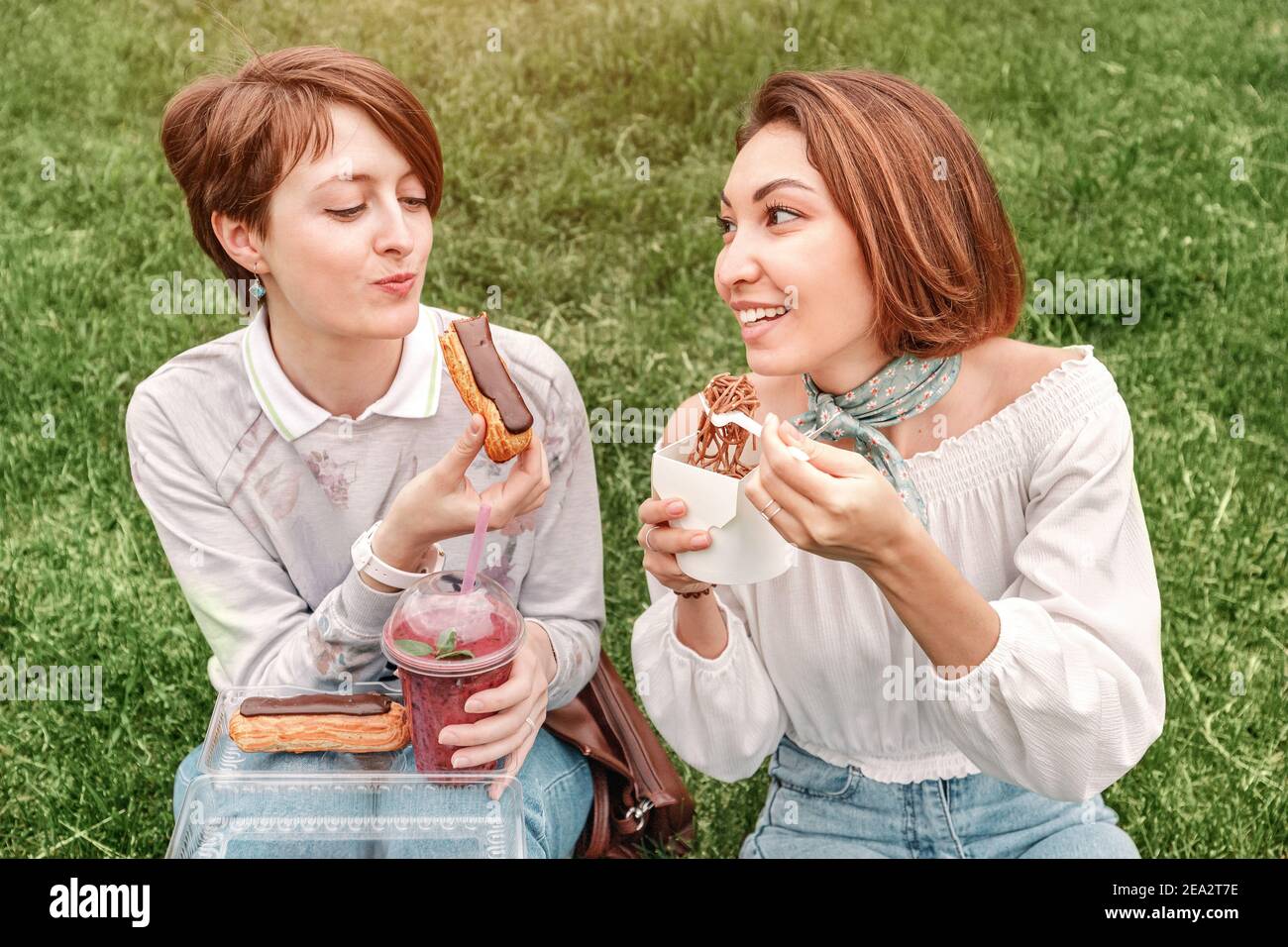 Deux filles amis faisant un pique-nique dans le parc de la ville sur l'herbe verte. Concept de communication et de nourriture de rue Banque D'Images