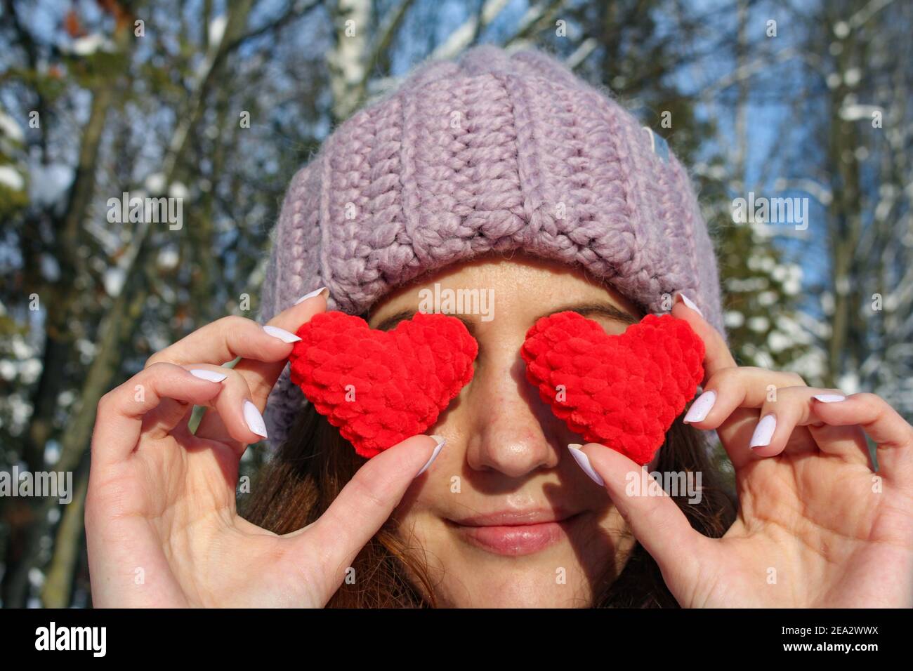 Saint Valentin, la fille couvre ses yeux avec des coeurs rouges tricotés comme symbole de l'amour Banque D'Images