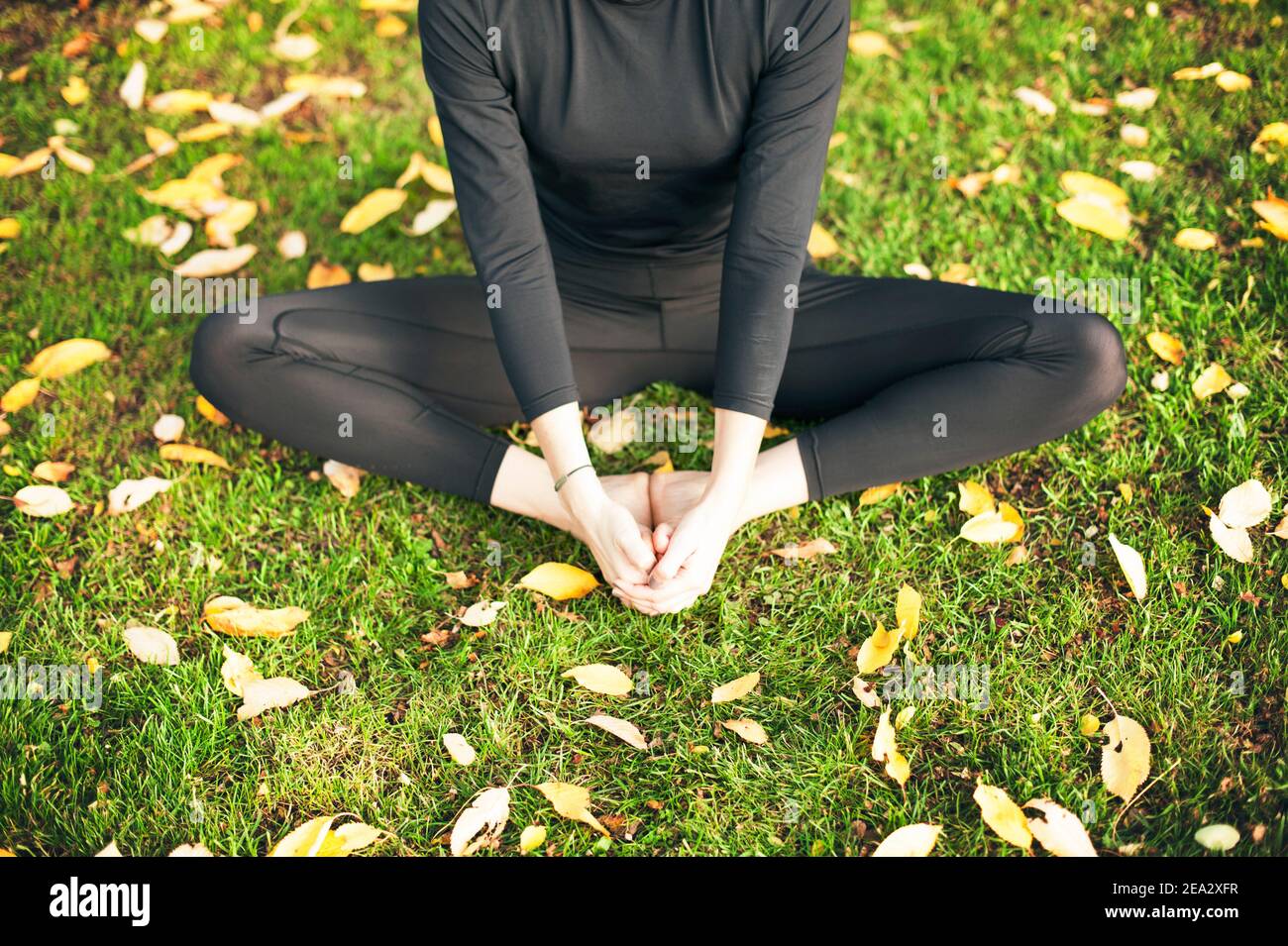 Femme faisant le yoga s'étirant à l'extérieur, mains tenant les pieds, assis sur l'herbe pieds nus, position papillon. Entraînement dans la nature, concept de style de vie sain Banque D'Images