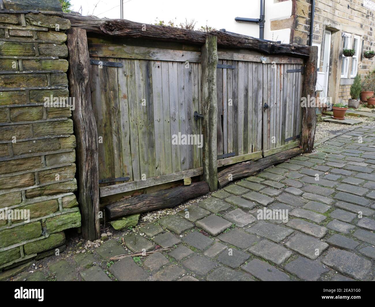 Route pavée à flanc de coteau ancienne découvrant de courtes portes en bois avec rugueux bois de rotage charpente par mur de pierre et maisons Banque D'Images
