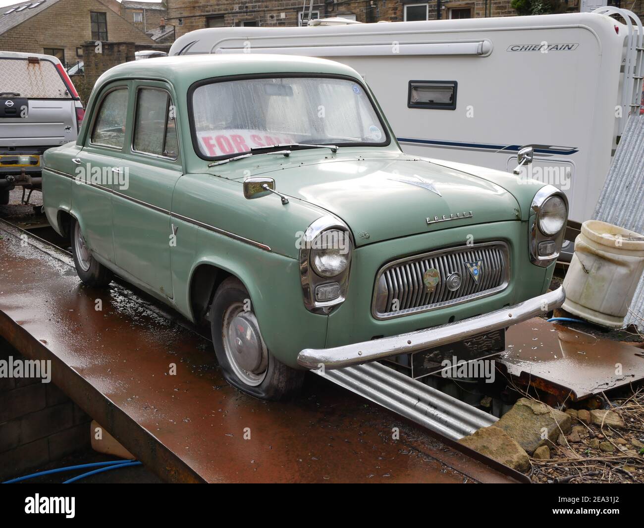 L'ancienne voiture verte à quatre portes du préfet se tenait sur des poutres métalliques avec caravane en arrière-plan Banque D'Images