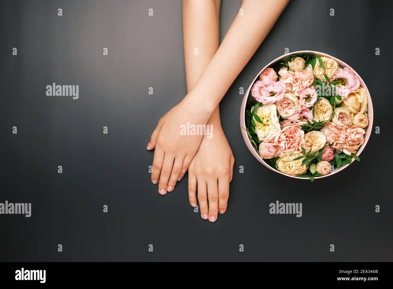 Boîte avec de belles fleurs à côté des mains de womans sur le fond noir avec espace de copie. Concept de carte salone beauté. Cadeau pour le 8 mars, Fête des mères Banque D'Images