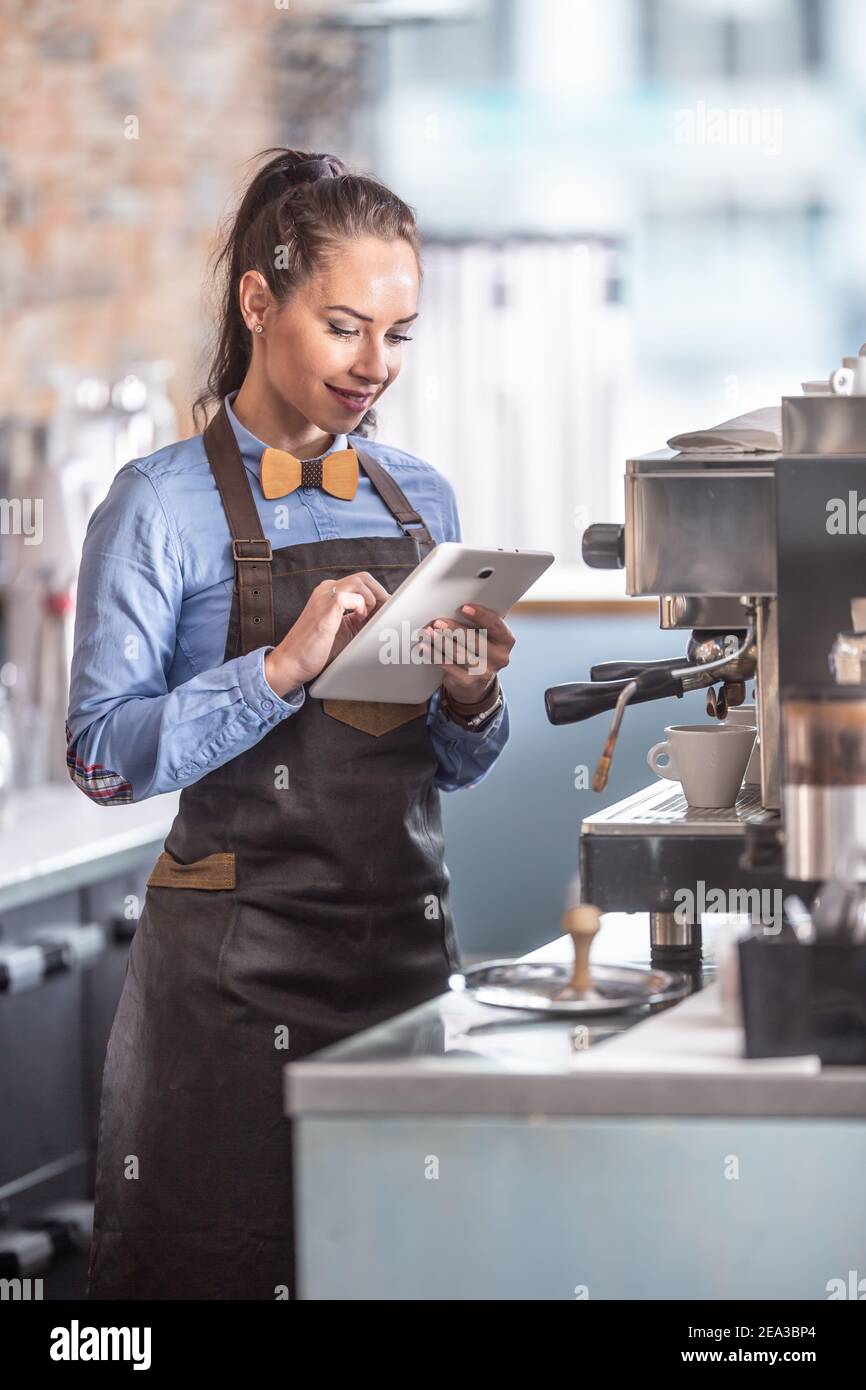 La serveuse utilise une tablette en attendant que les espressos soient terminés dans une cafetière. Banque D'Images