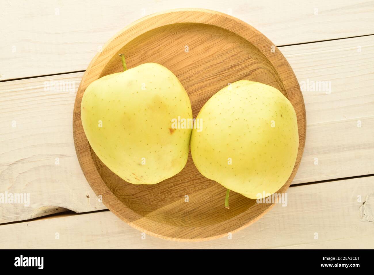 Deux pommes jaunes biologiques sur un plateau en bois rond, gros plan, sur une table en bois. Banque D'Images