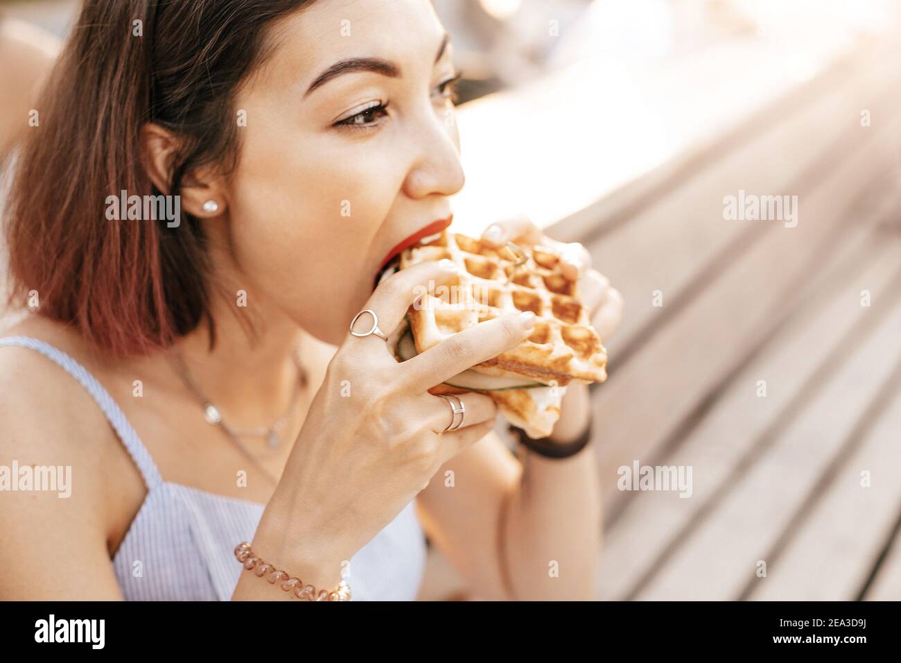 Femme hipster souriante mangeant un délicieux sandwich avec un pain d'une gaufre viennoise à carreaux. Concept de cuisine de rue moderne Banque D'Images