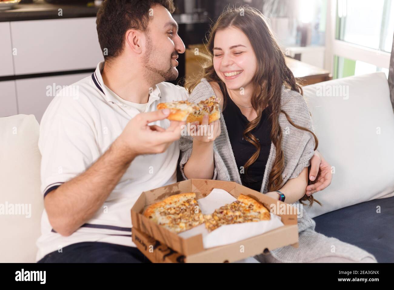 Couple heureux à la maison se nourrissant les uns les autres avec de la pizza. Banque D'Images