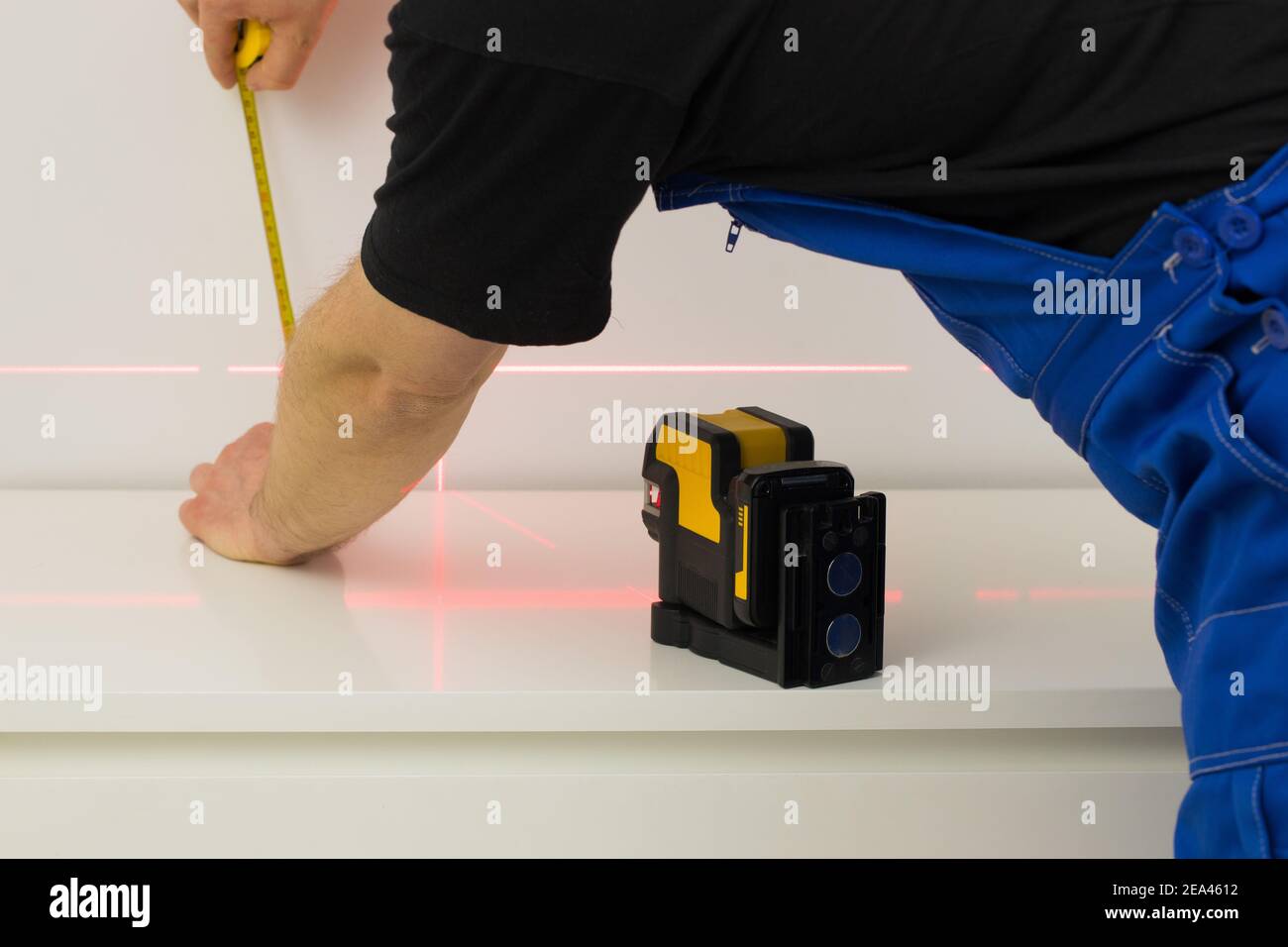 le spécialiste utilise un laser électronique pour vérifier les angles droits et les lignes lors de la prise de mesures de la pièce Banque D'Images