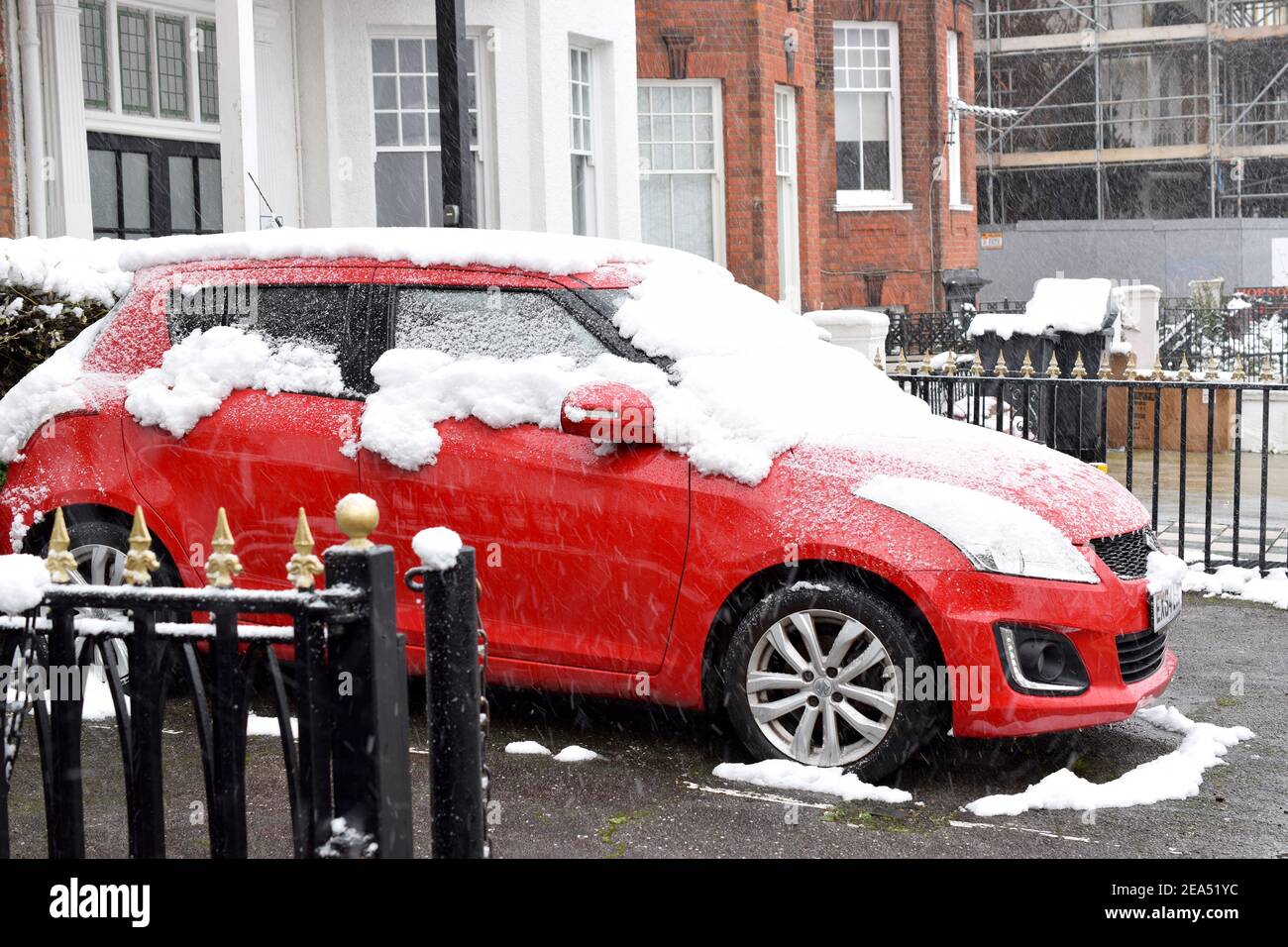 Vue sur la rue avec une voiture rouge couverte de neige sur la rue anglaise. Banque D'Images