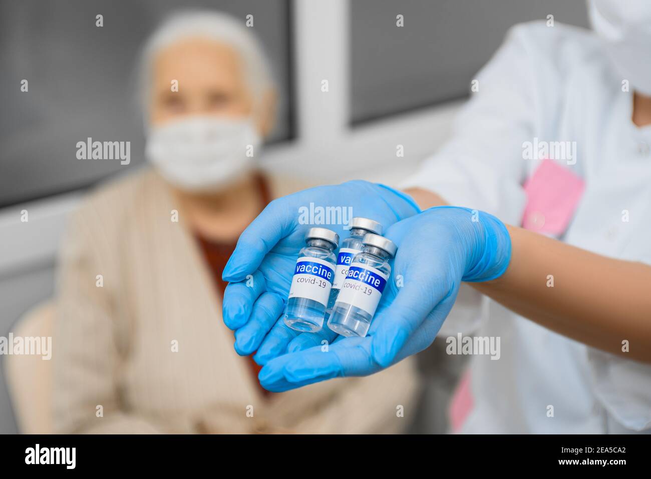 Flacons avec le vaccin Covid dans les mains d'un médecin sur le fond d'une femme âgée Banque D'Images