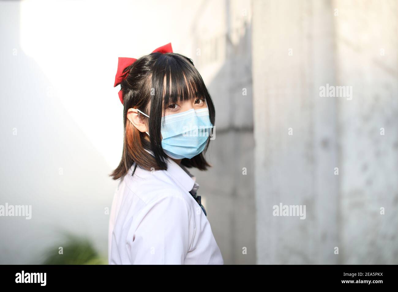 École asiatique fille avec masque dans la ville urbaine avec arbre arrière-plan Banque D'Images