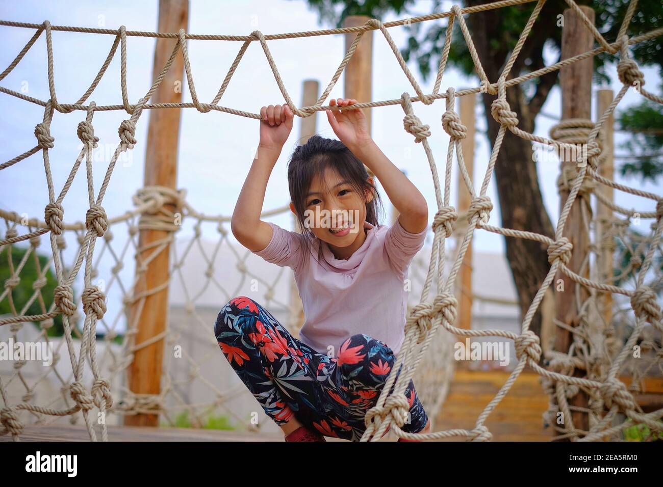 Une adorable jeune fille asiatique qui court le long d'un pont dans un terrain de jeu obstacle composé de cordes et de bois. Banque D'Images