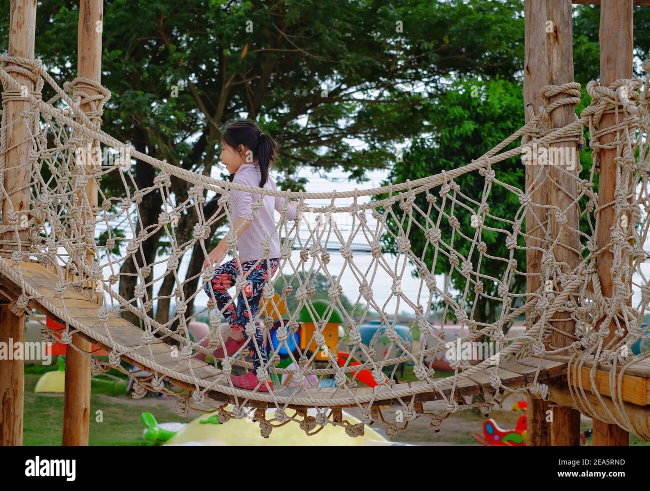 Une adorable jeune fille asiatique qui court le long d'un pont dans un terrain de jeu obstacle composé de cordes et de bois. Banque D'Images
