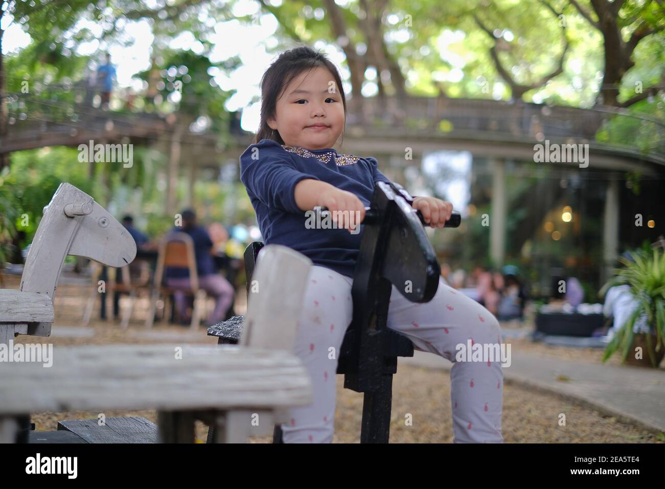Une jeune fille asiatique mignonne est à cheval rond-point en bois, souriant et s'amuser dans un parc. Banque D'Images