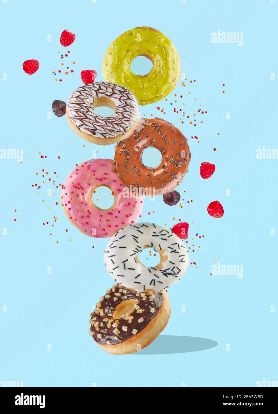 Lévitation alimentaire - beignets doux et colorés volant dans l'air avec des framboises et des saupoudriers colorés. Banque D'Images