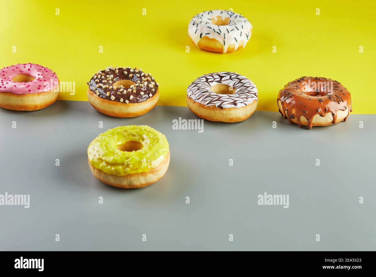 Beignets multicolores avec glaçure et saupoudrer sur un fond jaune-gris Banque D'Images