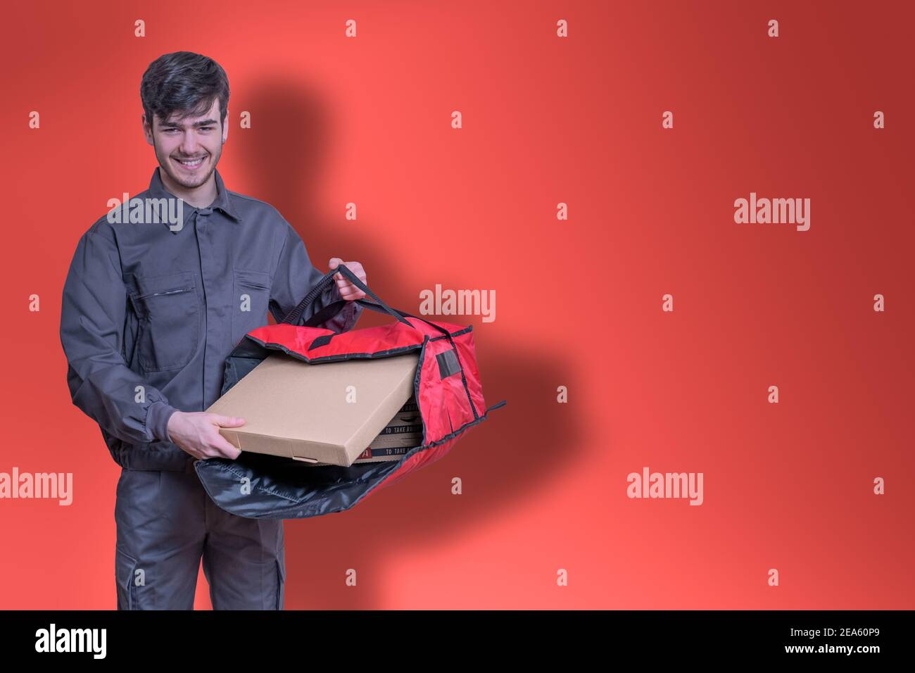 Livreur rapide de nourriture avec des boîtes à pizza dans ses mains livrant la commande pour la livraison, vêtu en uniforme et souriant, avec sac rouge Banque D'Images