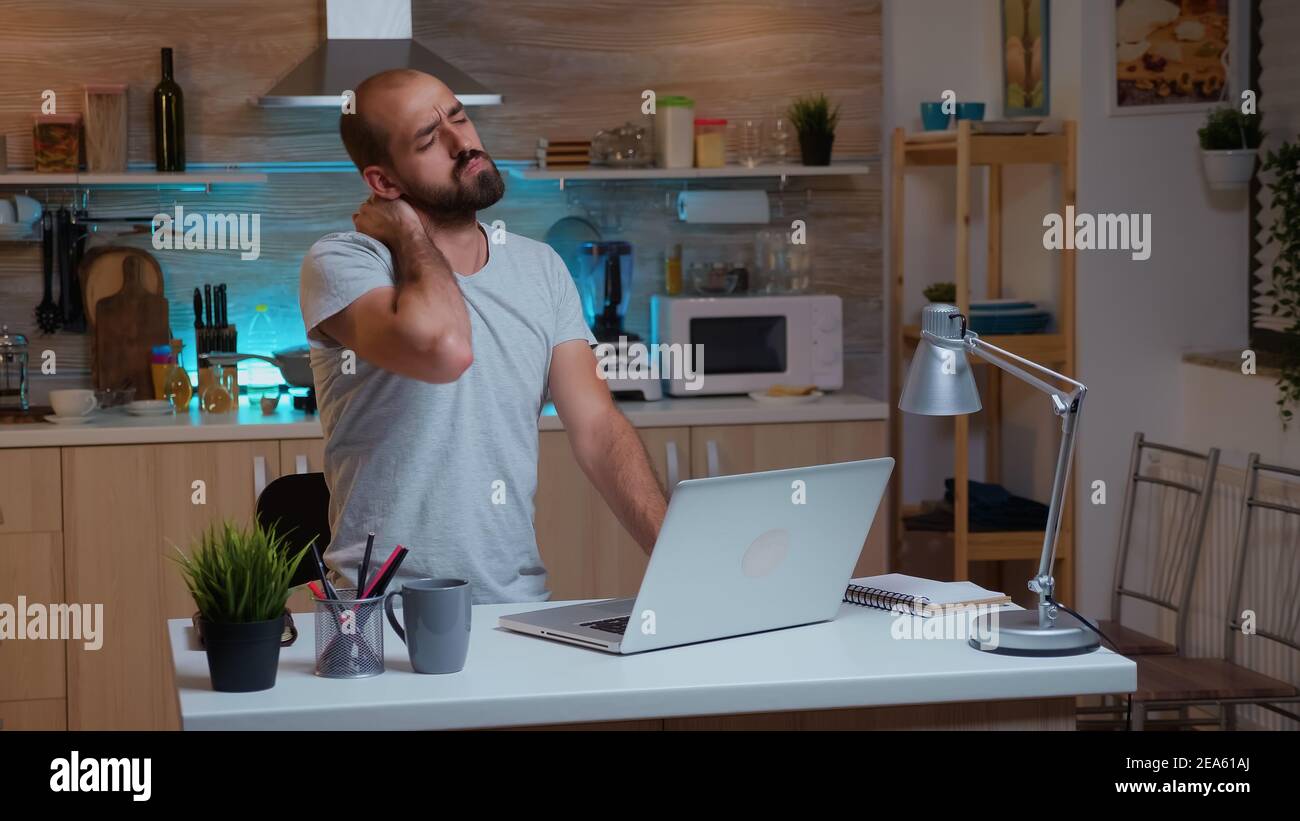 Un travailleur indépendant épuisé a fait un tour de cou tout en travaillant à une date limite tard dans la nuit. Employé occupé utilisant le réseau de technologie moderne sans fil faire des heures supplémentaires pour la lecture d'un travail écrit, la recherche Banque D'Images
