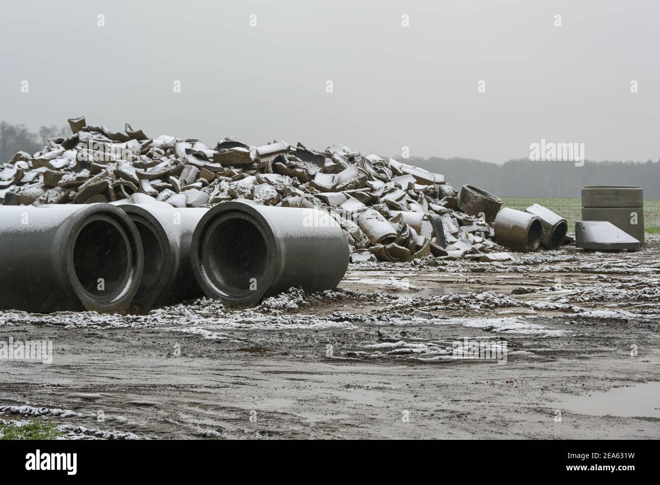 Tuyaux en béton cassés et neufs pour l'installation de drainage sur un chantier de construction dans le champ par une journée humide et enneigée, concentration sélectionnée, profondeur de fi étroite Banque D'Images
