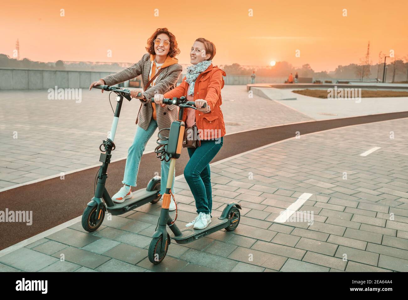 Deux amies se livrent à des scooters électriques modernes loués dans les rues de la ville. Transport et style de vie et amitiés concept Banque D'Images
