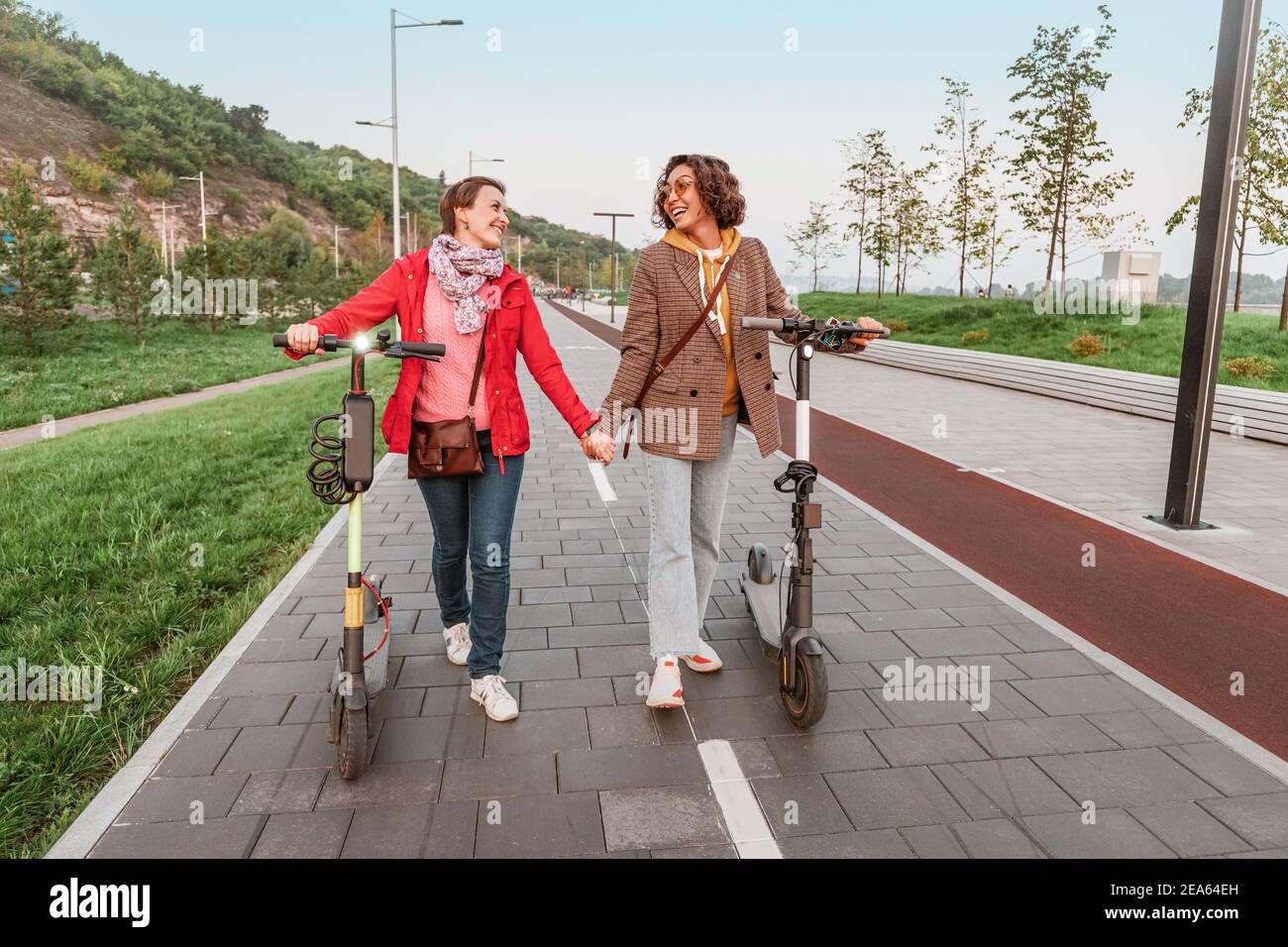 Deux amies se livrent à des scooters électriques modernes loués dans les rues de la ville. Transport et style de vie et amitiés concept Banque D'Images