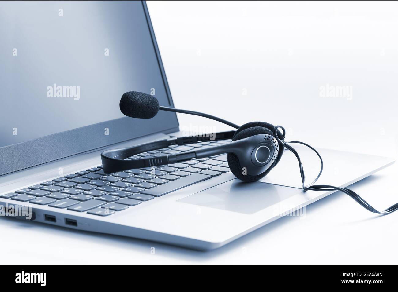 Ordinateur portable et casque sur fond blanc, ton bleu. Concept de centre d'appels, assistance, consultation. Banque D'Images