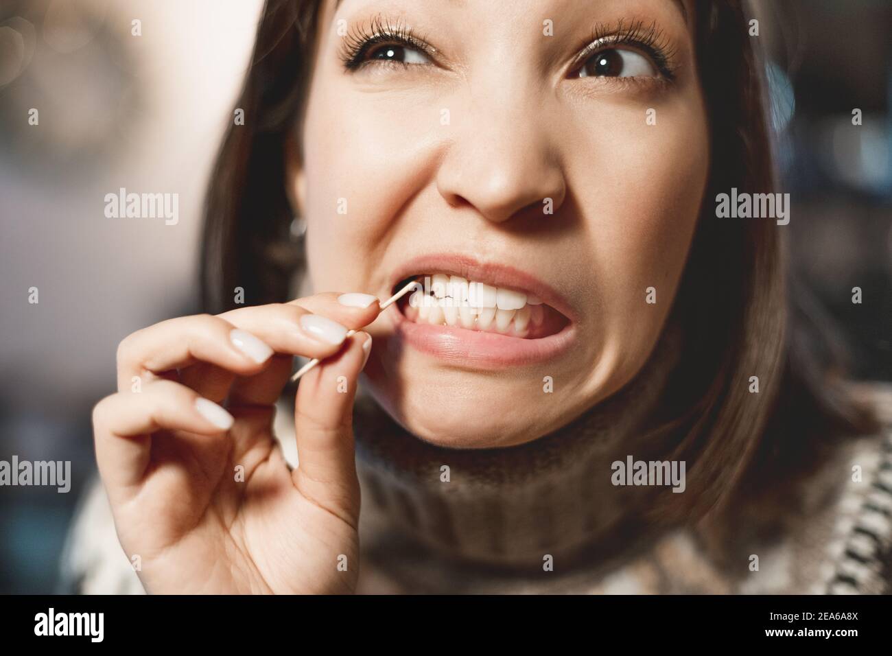 Une femme asiatique a un mal de dents après un grand repas et elle tire les restes de nourriture de la cavité dans ses dents avec un cure-dents. Le concept de denta Banque D'Images