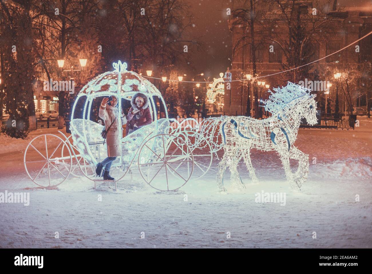Filles amis s'amusant dans le chariot de conte de fées illuminé avec des chevaux décorés de lumières et de guirlandes pour la nuit de Noël et les vacances du nouvel an. FR Banque D'Images