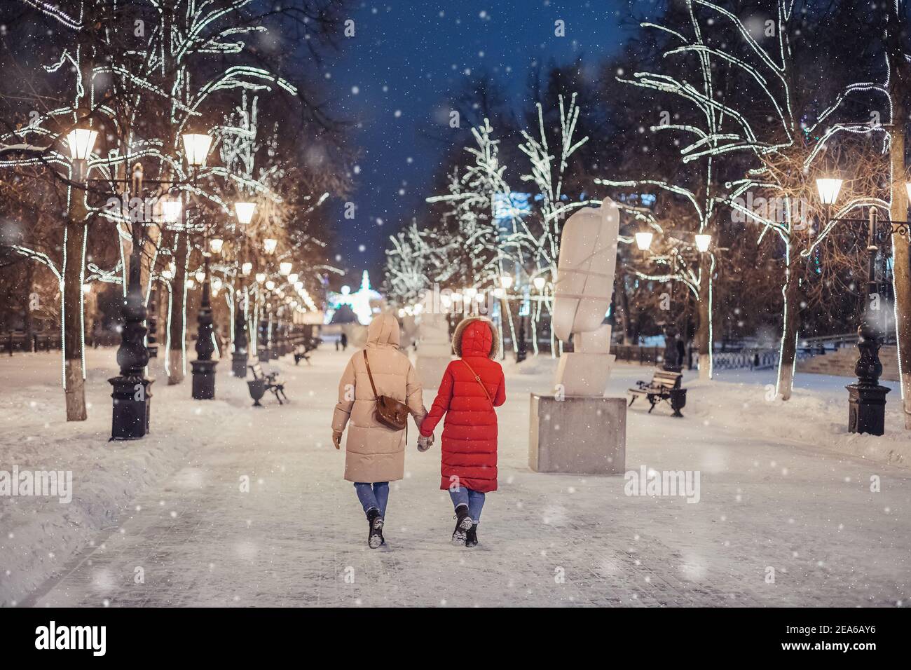 Des amies joyeuses marchent dans le parc d'hiver de la soirée sur le trottoir sur le fond des décorations de Noël et du nouvel an à Ufa, Russie Banque D'Images