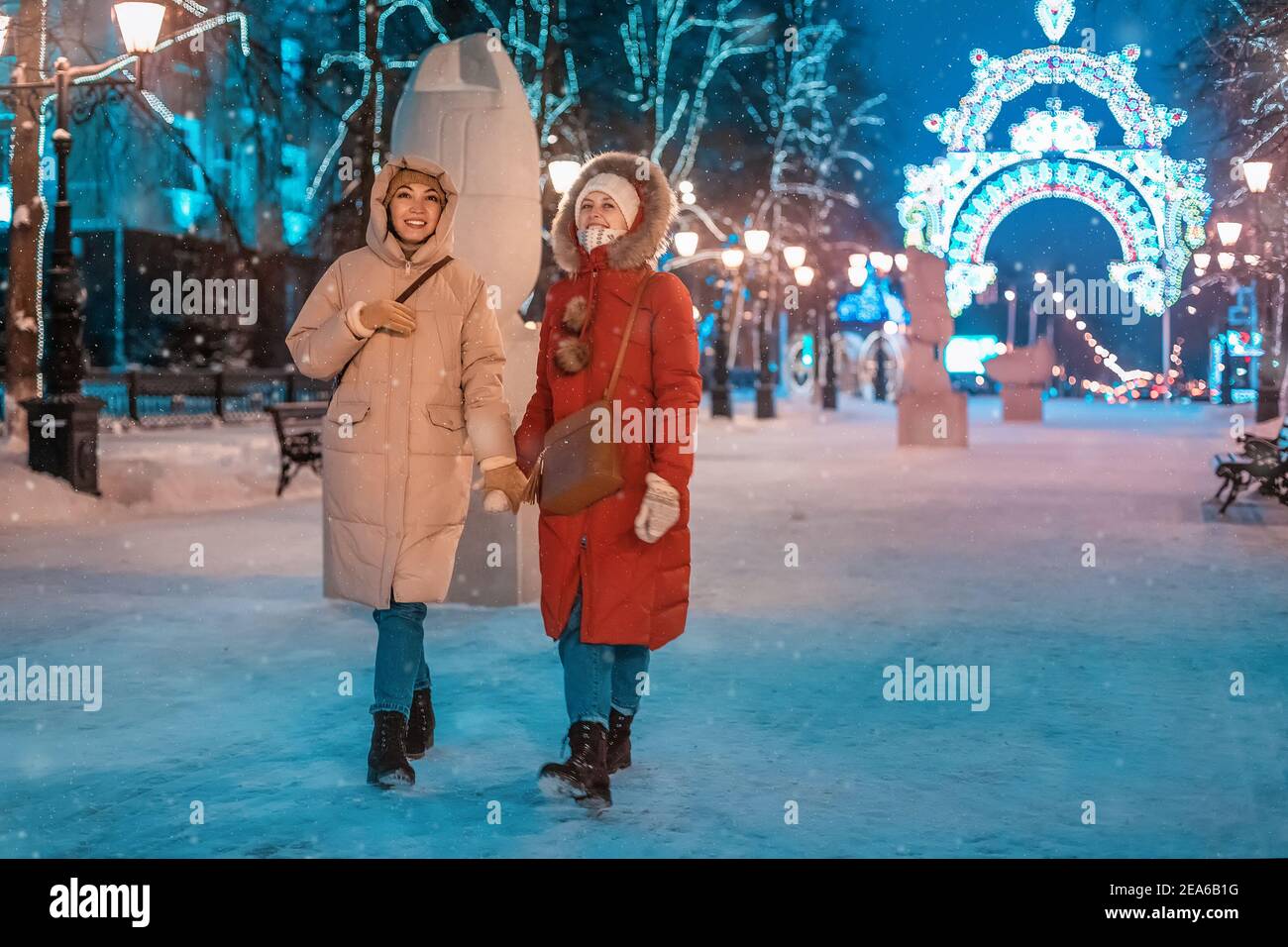 Des amies joyeuses marchent dans le parc d'hiver de la soirée sur le trottoir sur le fond des décorations de Noël et du nouvel an à Ufa, Russie Banque D'Images