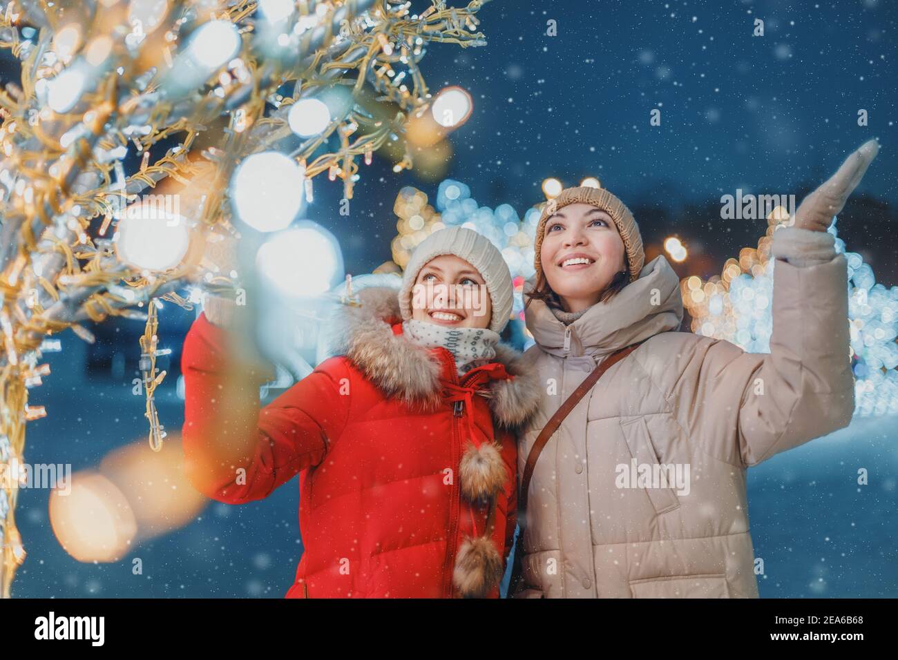 Filles amis s'amusant dans le centre-ville décoré avec des lumières et des guirlandes pour la nuit de Noël et les vacances du nouvel an. Amitié et concept de vacances Banque D'Images