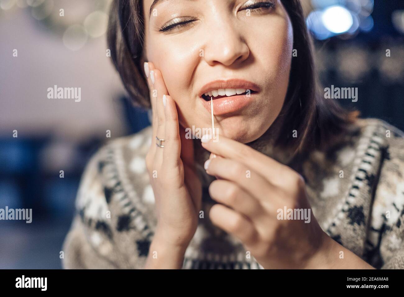 Une femme asiatique a un mal de dents après un grand repas et elle tire les restes de nourriture de la cavité dans ses dents avec un cure-dents. Le concept de denta Banque D'Images