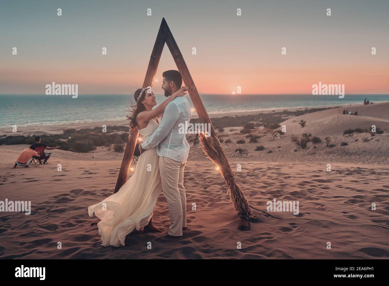 10 septembre 2020, Patara, Turquie : la mariée et le marié posent dans le désert au coucher du soleil sur la mer. Arc décoratif avec éclairage comme attribut pour une photo sho Banque D'Images