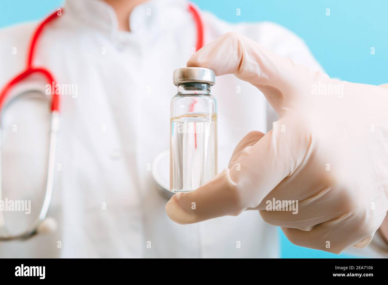 Covid 19 vaccin en flacon en verre flacon, médicament liquide en médecin main dans le gant avec stéthoscope. Injections de vaccination comme traitement sur bleu Banque D'Images