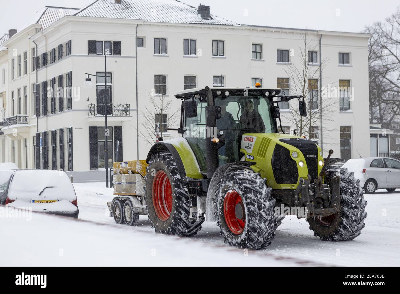 ZUTPHEN, PAYS-BAS - 07 février 2021 : tracteur vert après une forte chute de neige tirant un conteneur avec du sel pour réduire les routes glissantes Banque D'Images